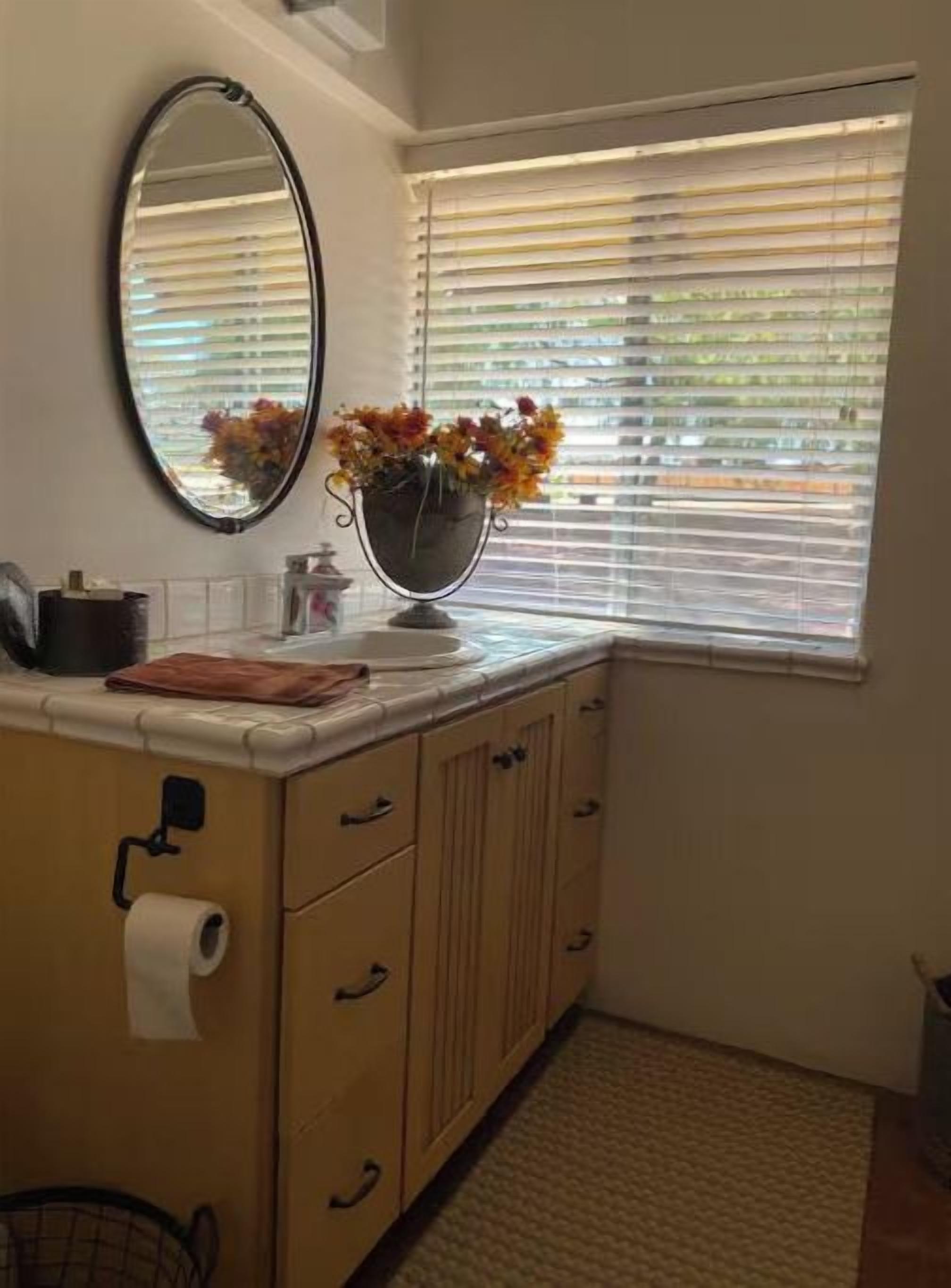 A bathroom with a sink, mirror, and window with blinds.