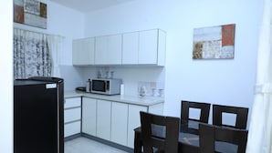 A compact kitchen with white cabinets, a microwave, and a dining area with dark chairs. - Anton White Villas Resort (Mahabalipuram)