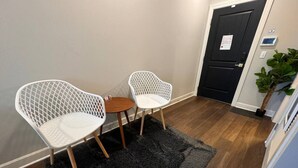 Een kamer met twee witte netstoelen, een klein houten tafeltje en een zwart vloerkleed op een houten vloer.