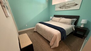 Een slaapkamer met een bed, nachtkastjes, een bankje en een decoratief stuk gemaakt van veren aan de muur.