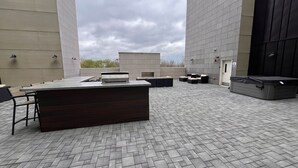 An outdoor terrace with a long table and chairs, surrounded by high walls and a cloudy sky. - Loft 207- Modern Condo with Rooftop Terrace Access (Lawrence)
