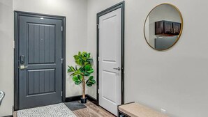 A hallway with a grey door, a white door, a small plant, a round mirror, and a bench with storage drawers. - Loft 207- Modern Condo with Rooftop Terrace Access (Lawrence)