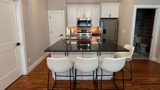 A modern kitchen with a central island, white bar stools, and pendant lighting. - The Carriage House in East Lawrence (Lawrence)