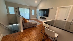 A modern kitchen with a central island, a dining area with bar stools, and a cozy seating area with a sofa and a fireplace. - The Carriage House in East Lawrence (Lawrence)