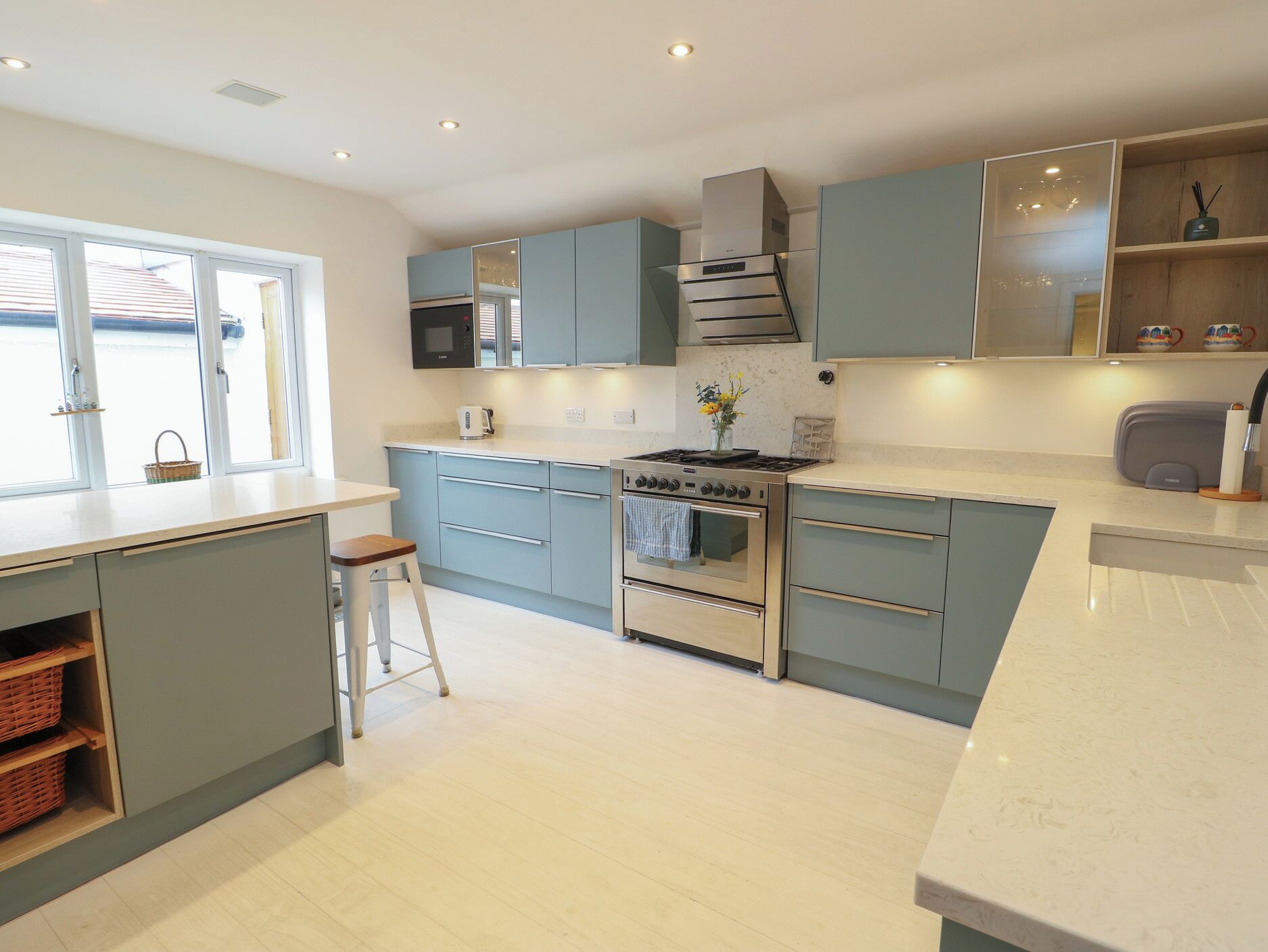 A modern kitchen with light blue cabinets, a stainless steel stove, and a large window.