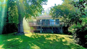 Una casa de dos pisos amb un balcó, envoltada de vegetació abundant i arbres.