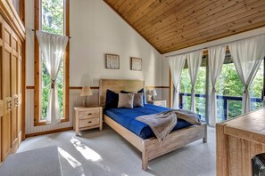 Dormitorio con estructura de madera, cama, mesitas de noche y vistas a la vegetación a través de amplias ventanas.