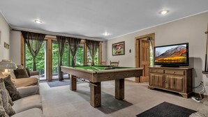 A pool table in a room with a sofa, a television, and a door leading outside. - Secluded EVL Getaway with Hot tub, Sauna, Fire Pit, Gym & Game room (Ellicottville)