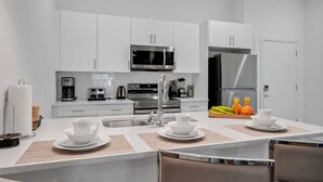 A modern kitchen with white cabinetry, stainless steel appliances, and a breakfast bar with seating. - Disney Dreams Cozy Pool Villa (Davenport)