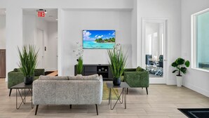 A modern living room with a large flat-screen TV, green upholstered sofas, and potted plants. - Disney Dreams Cozy Pool Villa (Davenport)