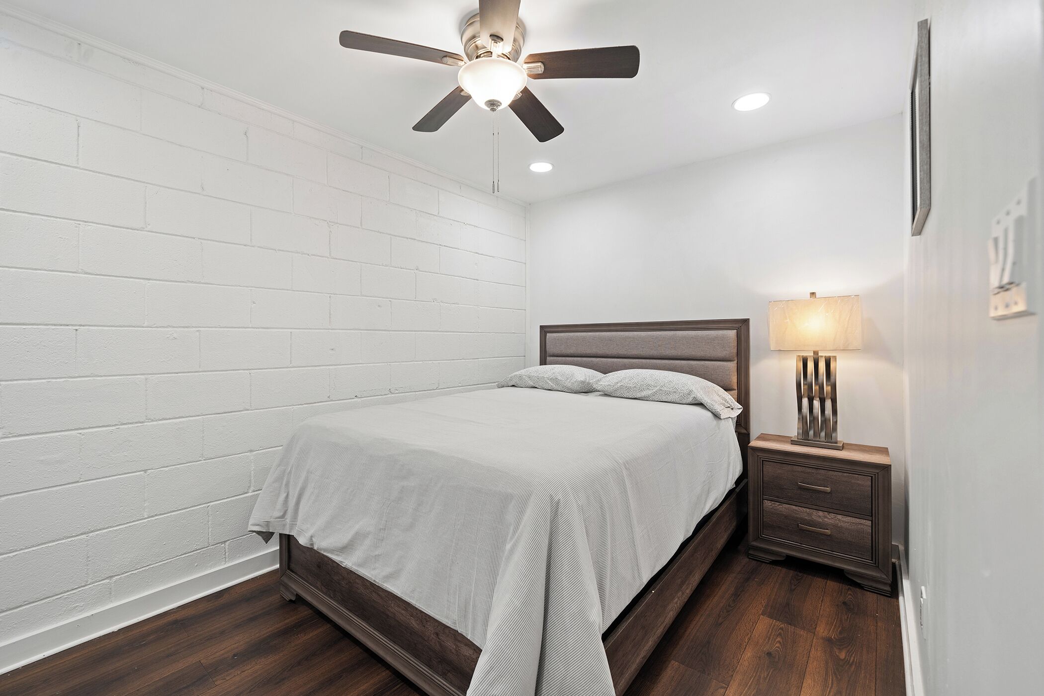 A bedroom with a bed, a nightstand, a lamp, and a ceiling fan.