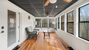 A sunroom with a wooden floor, large windows, a ceiling fan, and a seating area with a table. - Secluded PoolHouse Estate (College Park)