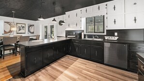 A modern kitchen with dark cabinetry, a large island, and pendant lighting. - Secluded PoolHouse Estate (College Park)