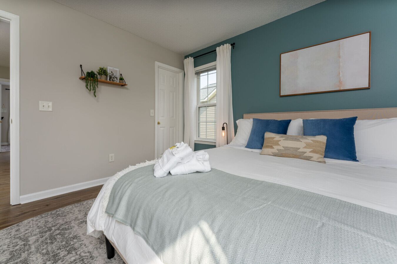 Une chambre à coucher avec un grand lit, une table de chevet, une étagère murale ornée de plantes et une fenêtre avec des rideaux.