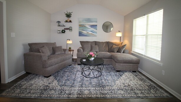A living room with two sofas, a coffee table, a painting, and a window with blinds. - Simple Stay at Spring Meadow (Valdosta)