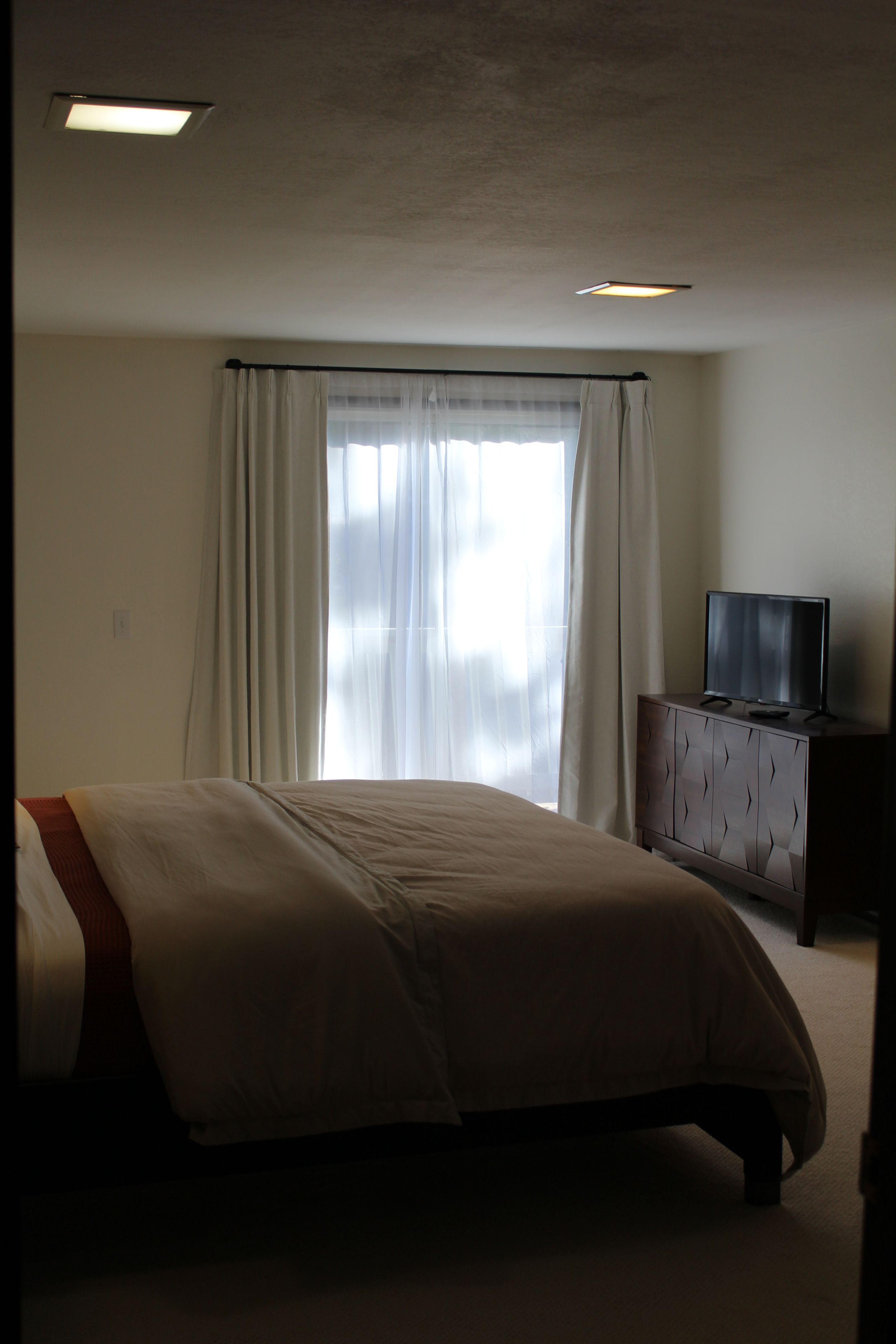 A hotel room with a bed, a television on a wooden cabinet, and a window with curtains.