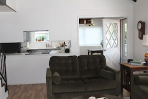 Uma sala de estar com um sofá verde escuro, uma mesa de centro de madeira e uma área de cozinha com uma janela.