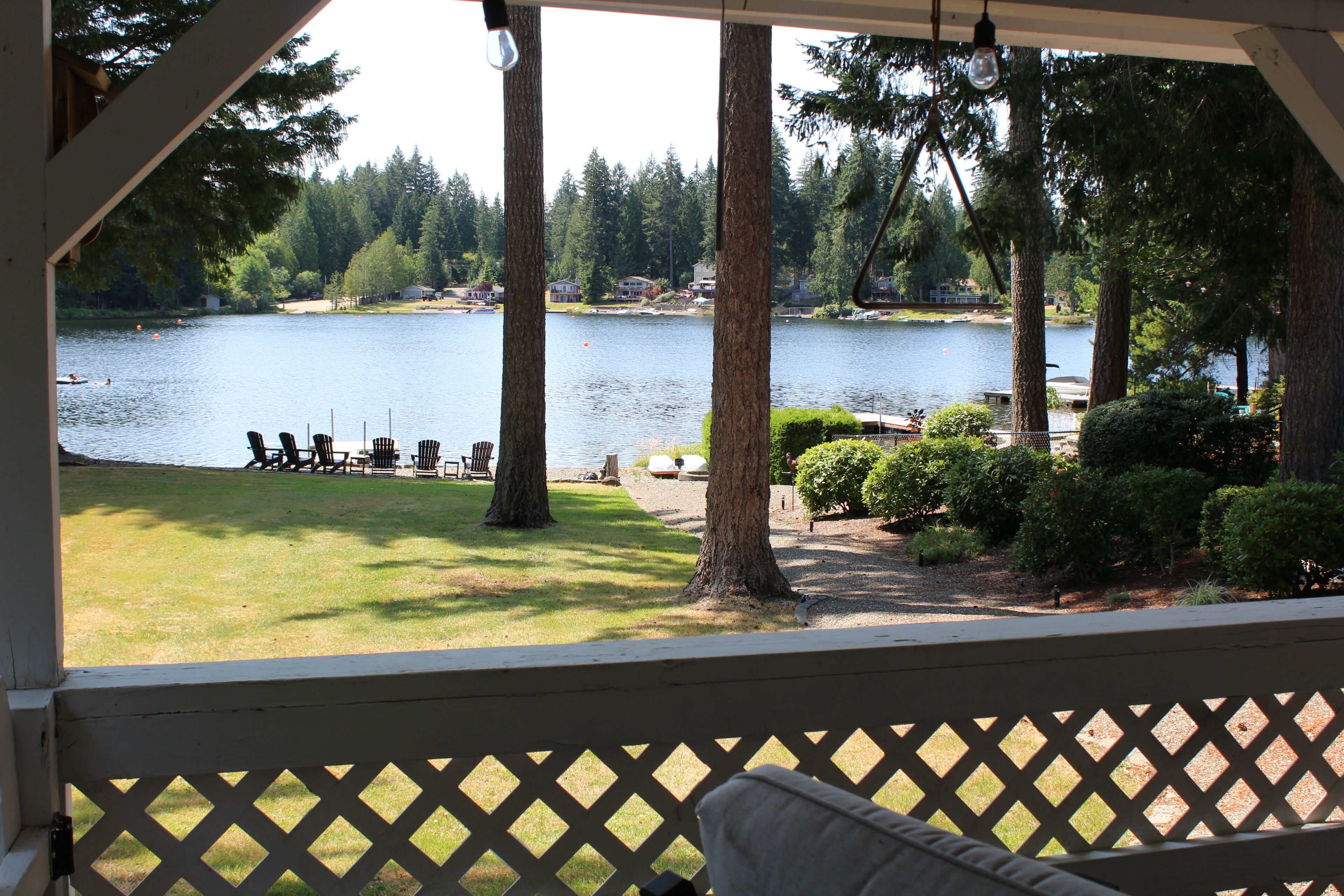 A lakeside view from a covered deck with a seating area and a view of the lake and surrounding trees.