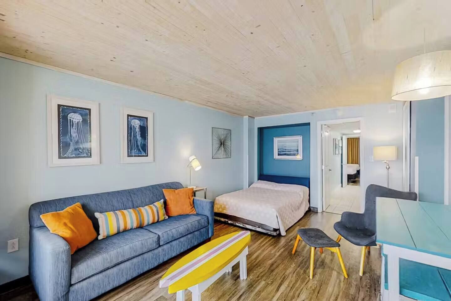 A room with a blue sofa, a bed, a desk, and a bench.