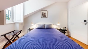 Een slaapkamer met een bed, een raam, een deur en een klein tafeltje met een lamp.