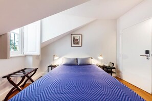 Une chambre à coucher avec un lit, une fenêtre, une porte et une petite table avec une lampe.