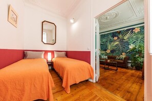 A room with two beds, a mirror, and a door leading to a living area with a tropical wallpaper. - Contador Mor Rooms and Apartments (Lisbon)