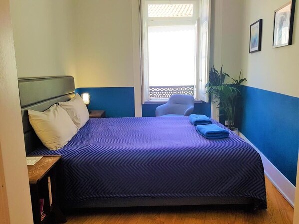 A bedroom with a bed, a nightstand, a chair, and a window with a view.