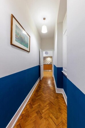 A hallway with blue and white walls, wooden flooring, a framed picture on the wall, and a door at the end. - Contador Mor Rooms and Apartments (Lisbon)