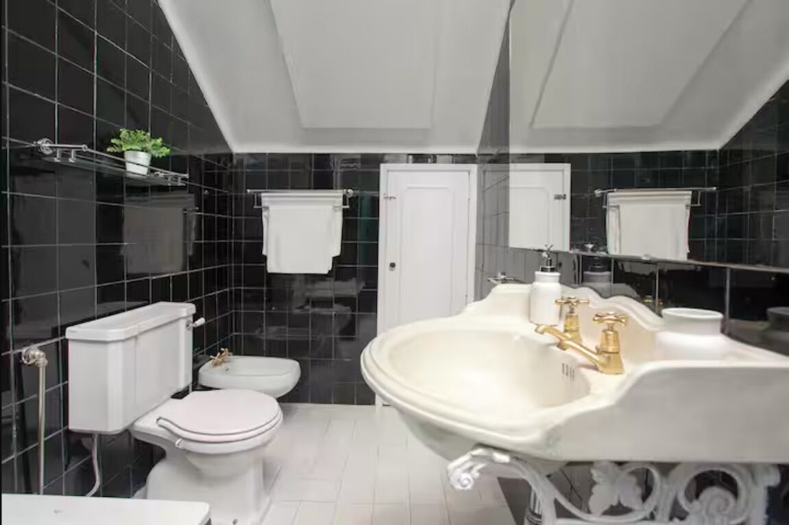 A bathroom with a white toilet, a sink with gold fixtures, and a mirror above the sink.