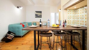 Een moderne woonkamer met een blauwgroene bank, een houten eettafel met barkrukken, en een keuken met patroon betegelde vloeren.