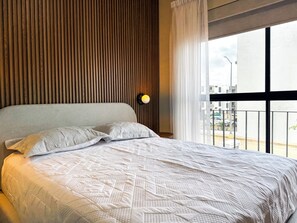 Un dormitorio con cama, pared de listones de madera, ventana con vistas y luz empotrada.