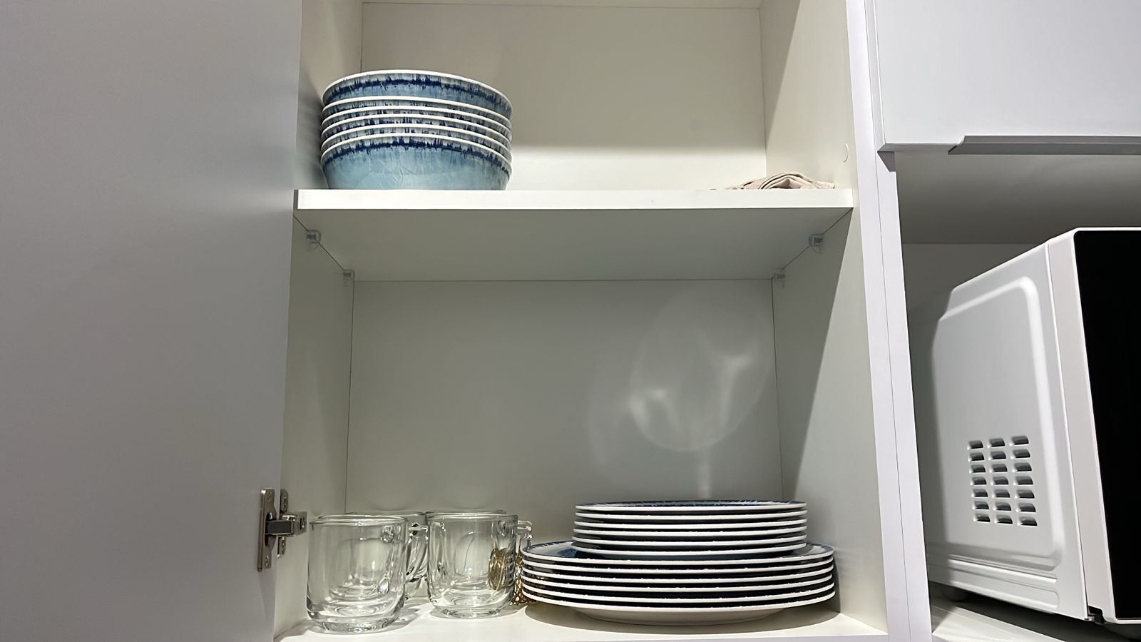 A kitchen cabinet with stacked plates and clear glass mugs.