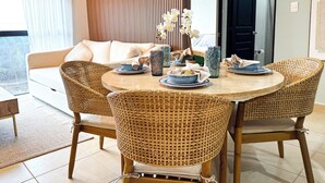 Een eetgedeelte met een ronde tafel, rieten stoelen en een bank op de achtergrond.