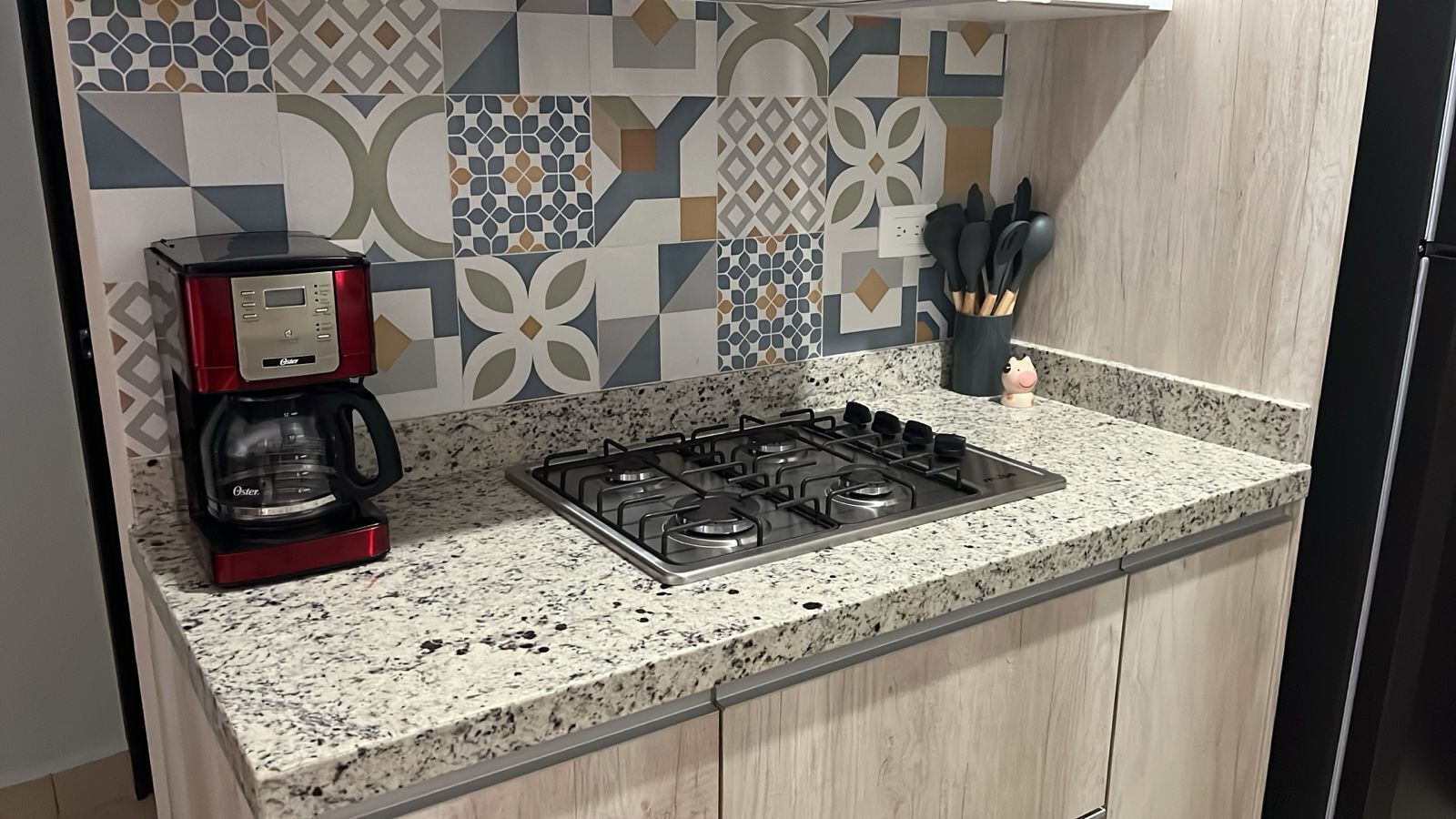 A kitchen with a gas stove, a coffee maker, and a backsplash with geometric patterns.