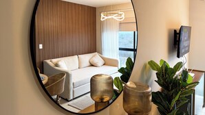 Een moderne woonkamer met een bank, een ronde spiegel, een televisie en een groot raam.