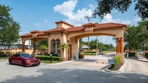 A building with a red-tiled roof, a covered entrance, and a red car parked in front. - Bella Vida Resort Home in Kissimmee (Kissimmee)