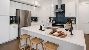 A modern kitchen with white cabinetry, stainless steel appliances, a central island with stools, and a blue herringbone backsplash. - Madmen Loft w/ Uptown Rooftop Views (Charlotte)