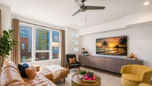 A modern living room with a leather sofa, a yellow armchair, a black leather chair, a round coffee table, and a large painting of a sunset. - Madmen Loft w/ Uptown Rooftop Views (Charlotte)