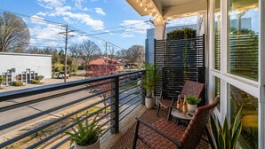 A balcony with a chair, table, and potted plants. - Madmen Loft w/ Uptown Rooftop Views (Charlotte)