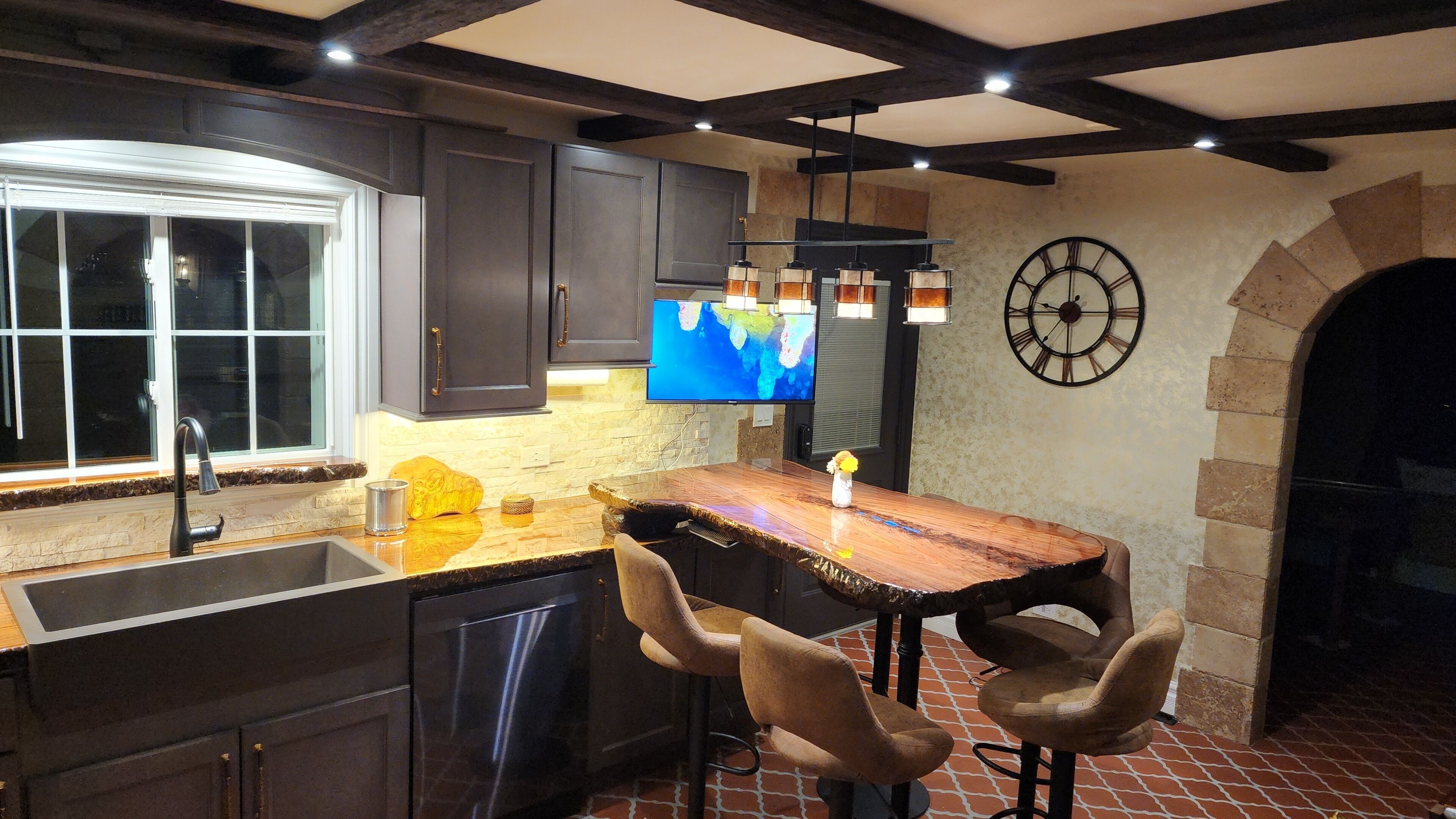 A kitchen with dark cabinets, a wooden bar counter, and a large clock on the wall.