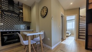 A modern kitchen with a dining area, a clock on the wall, and a staircase leading to another room. - Syncron Rooftop City Centre Tirana (Tirana)