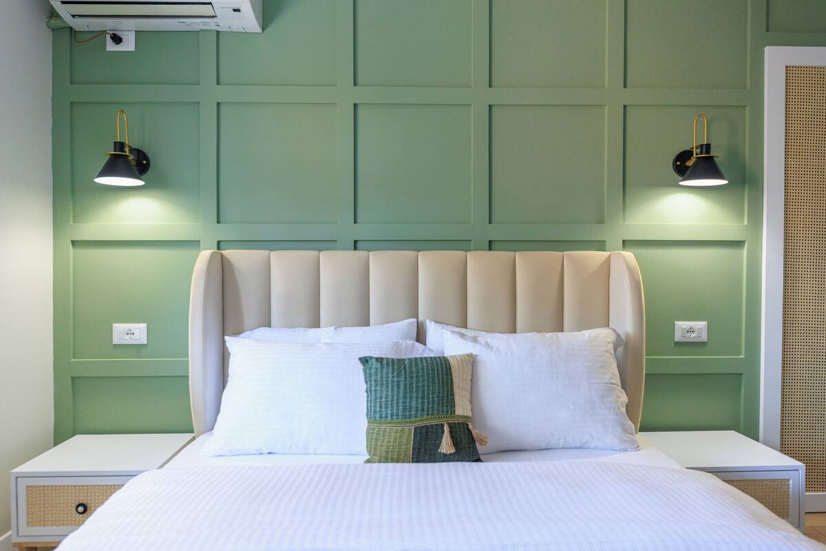A neatly made bed with a headboard, two bedside lamps, and a green accent pillow.