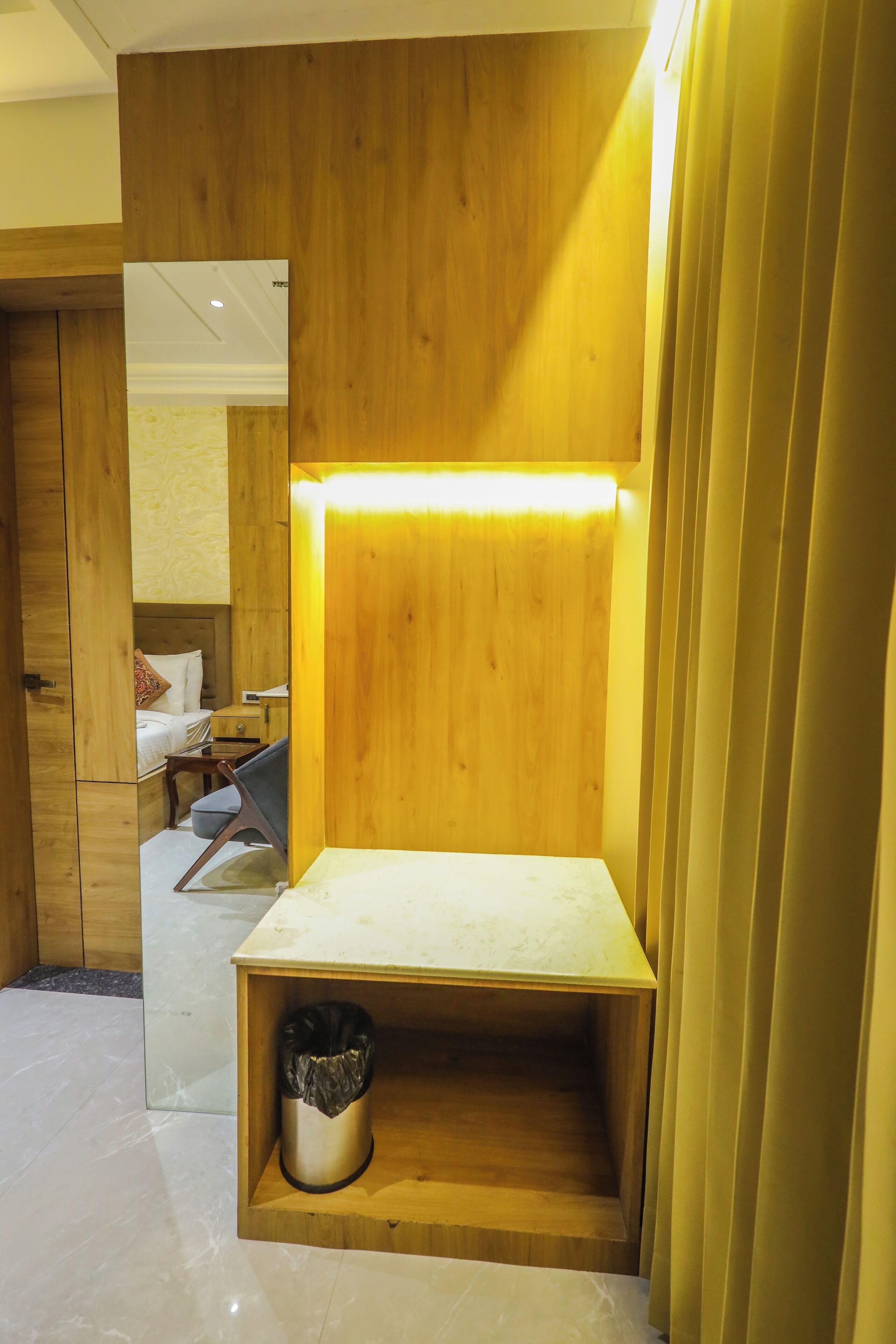 A room with a wooden desk, a trash bin, and a bed with a headboard.
