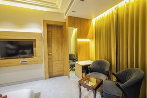 Habitación de hotel con pared de madera, televisor de pantalla plana montado sobre un mueble de madera, escritorio con silla y ventana grande con cortinas amarillas.