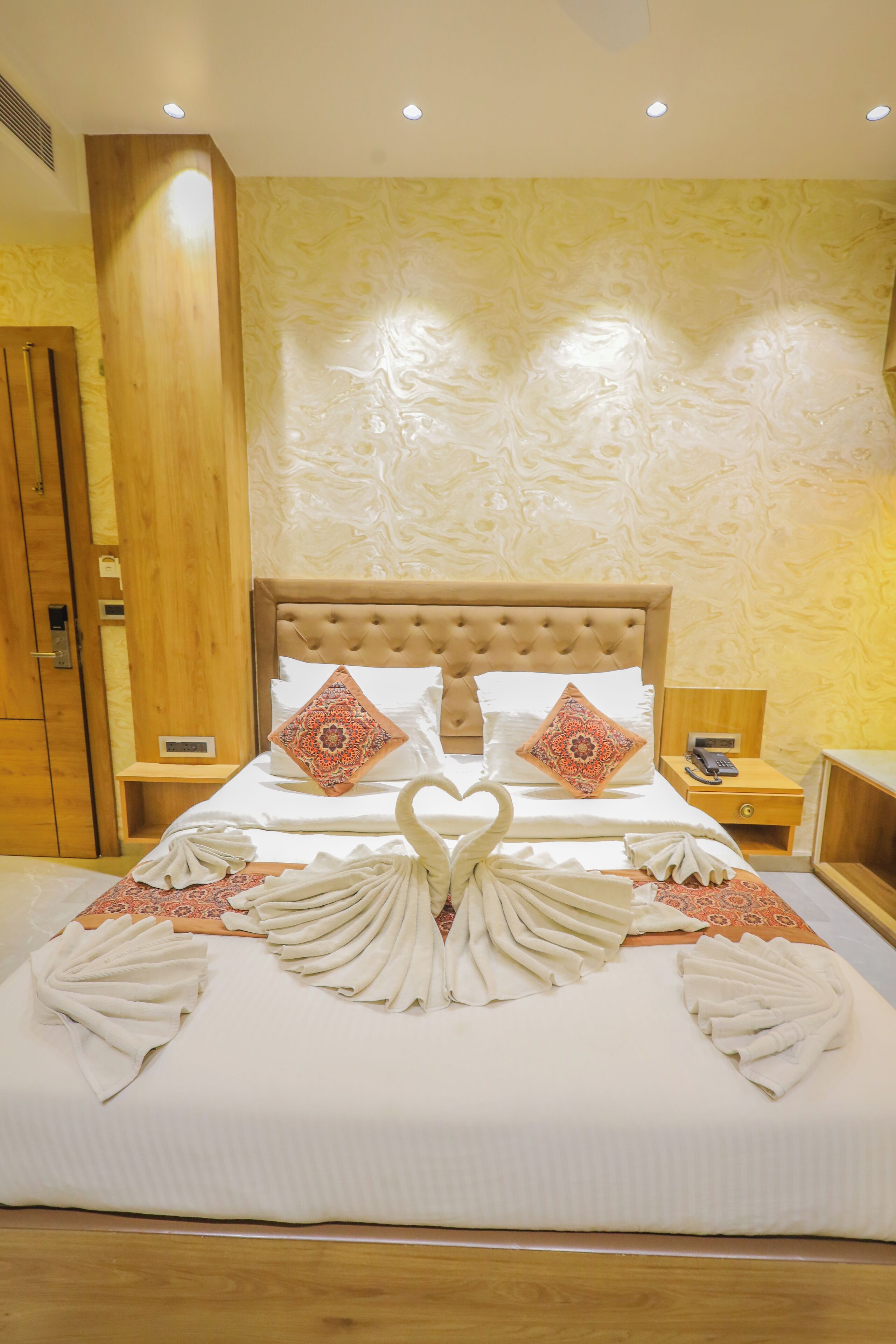 Un letto rifatto con cura, asciugamani decorativi disposti a forma di cigno, una testiera in legno e una parete decorata.