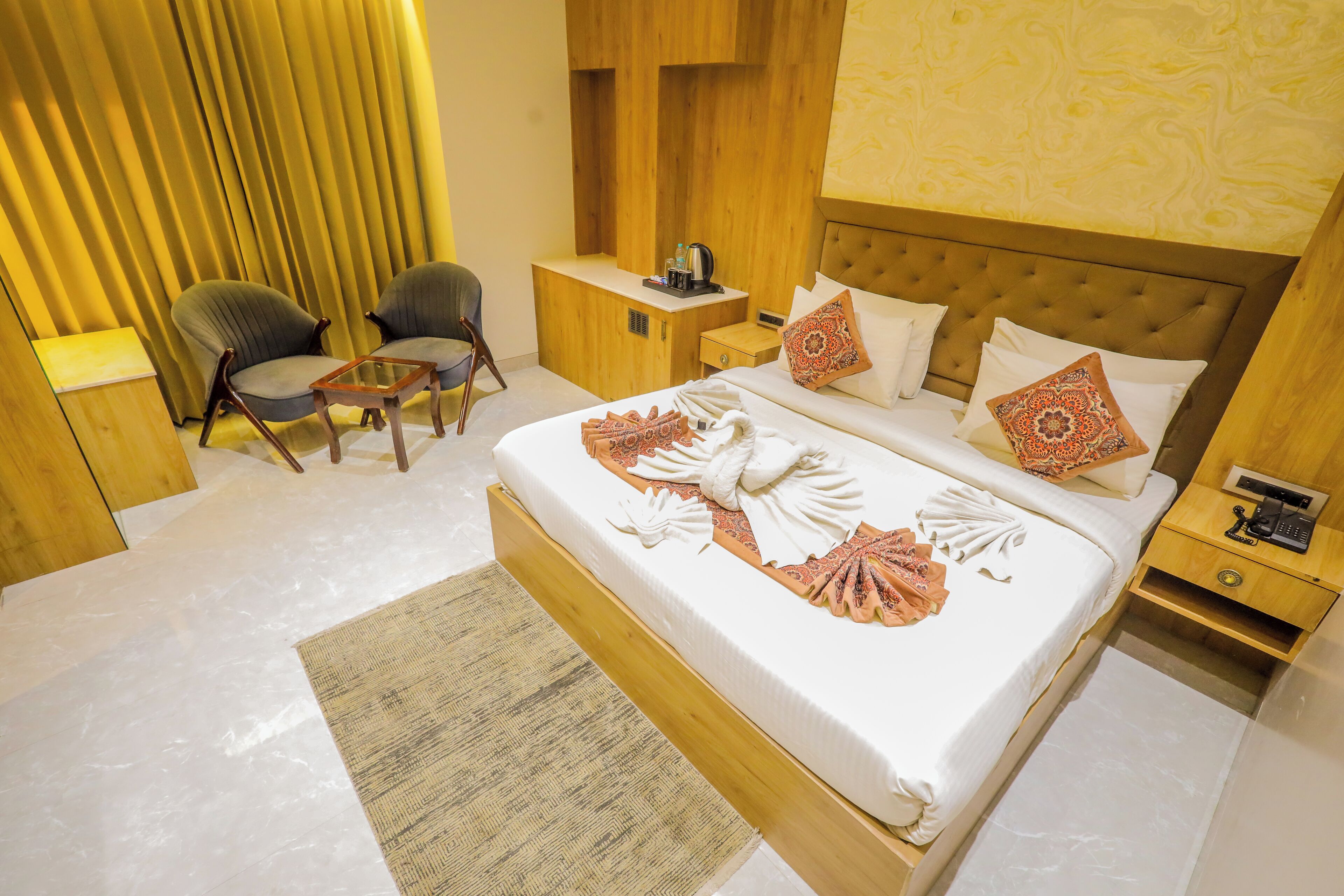 A hotel room with a large bed, two chairs, a wooden desk, and a nightstand.