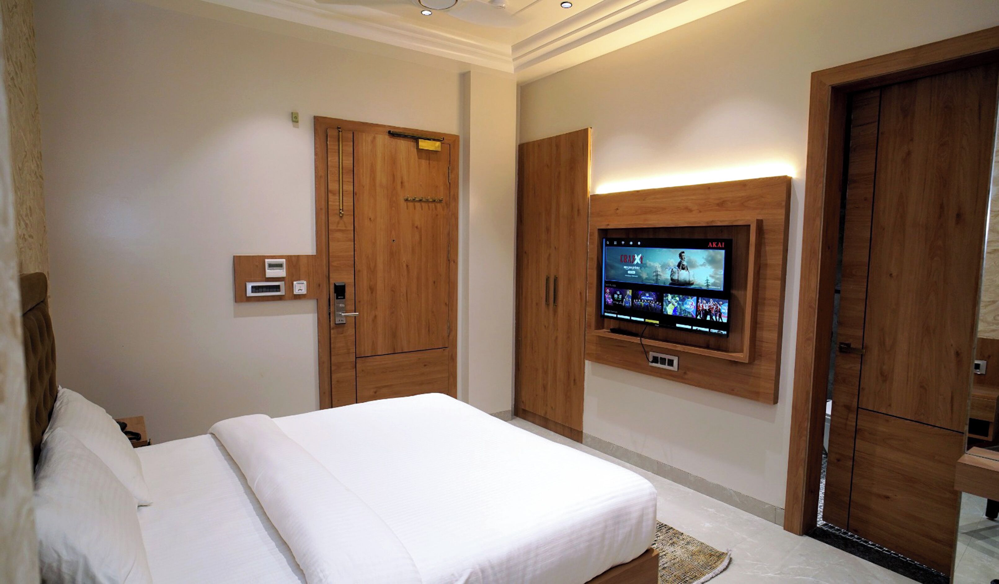 A hotel room with a large bed, wooden wardrobe, a built-in TV, and a thermostat on the wall.