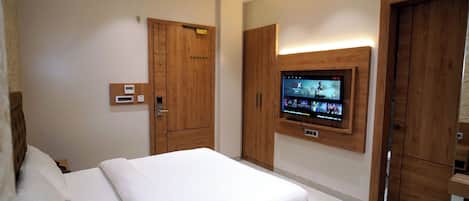 A hotel room with a large bed, wooden wardrobe, a built-in TV, and a thermostat on the wall.