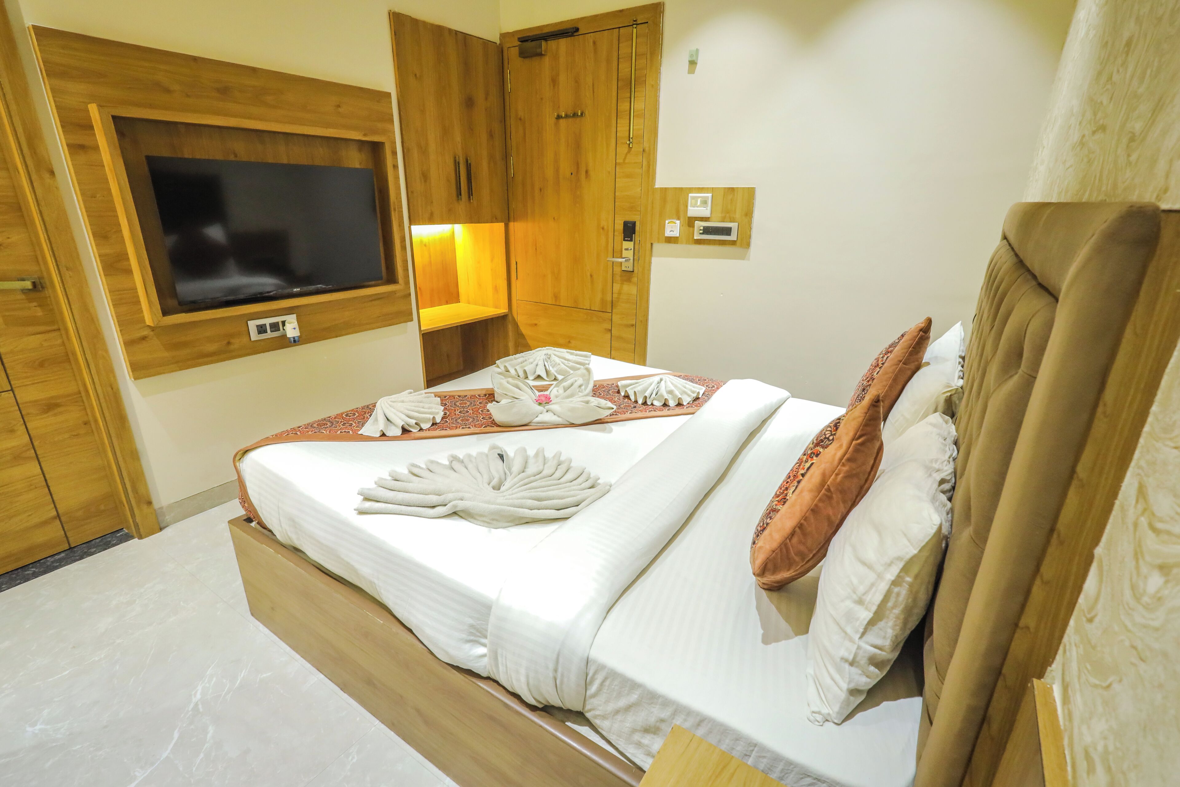 A hotel room with a wooden bed, a TV mounted on the wall, and a wooden wardrobe.