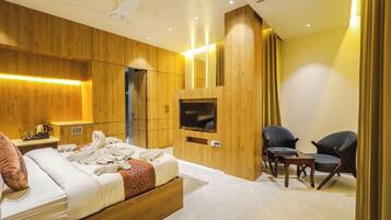 Un dormitorio moderno con cabecera de madera, televisor de pantalla plana, mesita de noche con lámpara y dos sillas.